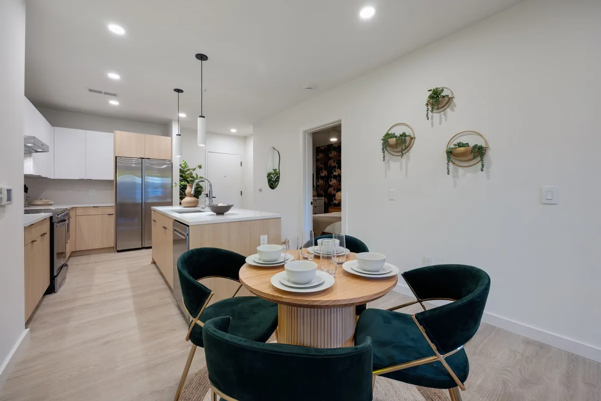 A stylish dining area set for four, adjacent to a modern kitchen island and surrounded by greenery accents. The space exudes warmth and is ready for shared meals or celebratory gatherings.
