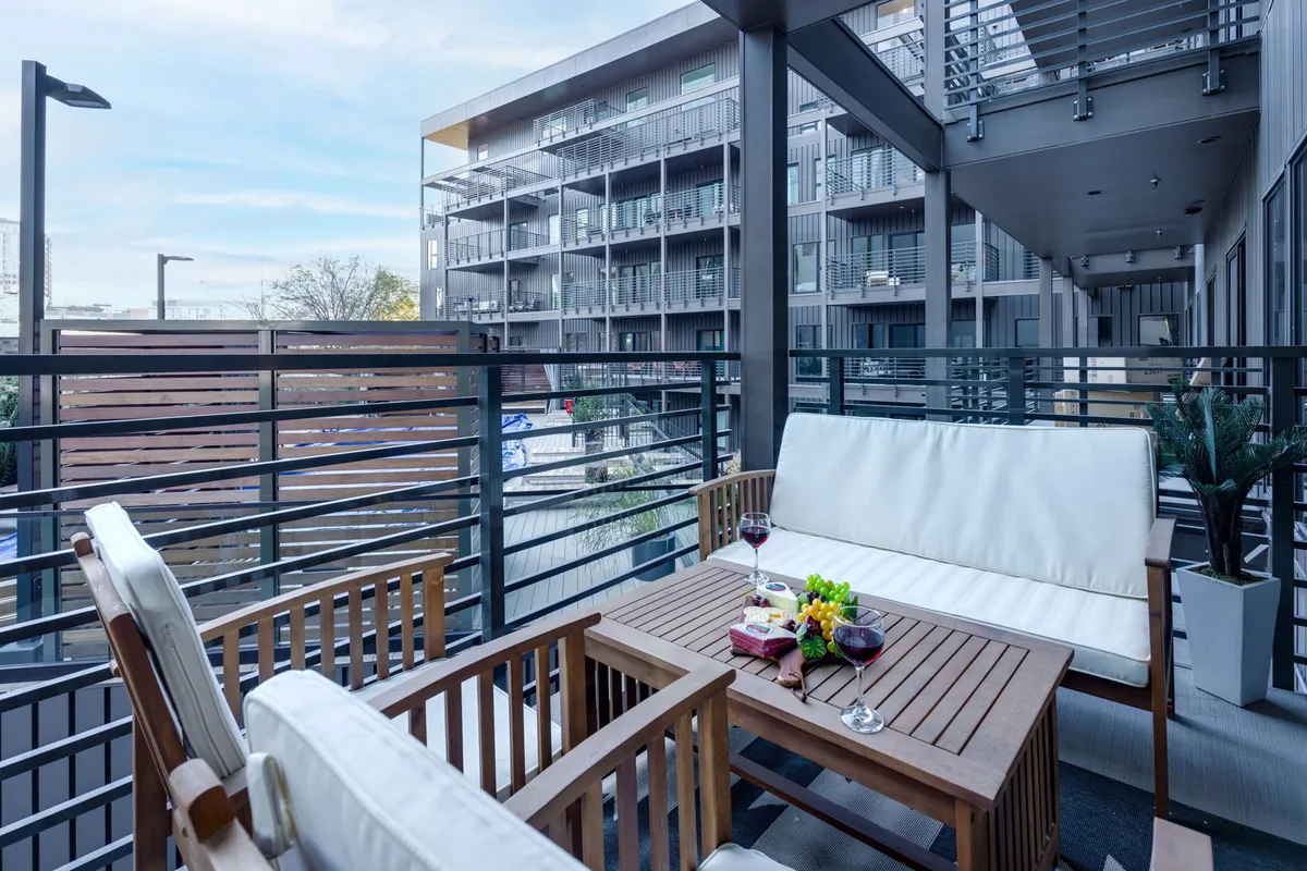 A cozy and stylish outdoor seating area featuring comfortable chairs, a table set with wine glasses and a snack platter, surrounded by decorative plants. The space is ideal for evening relaxation, drinks, and casual conversations under the city sky.