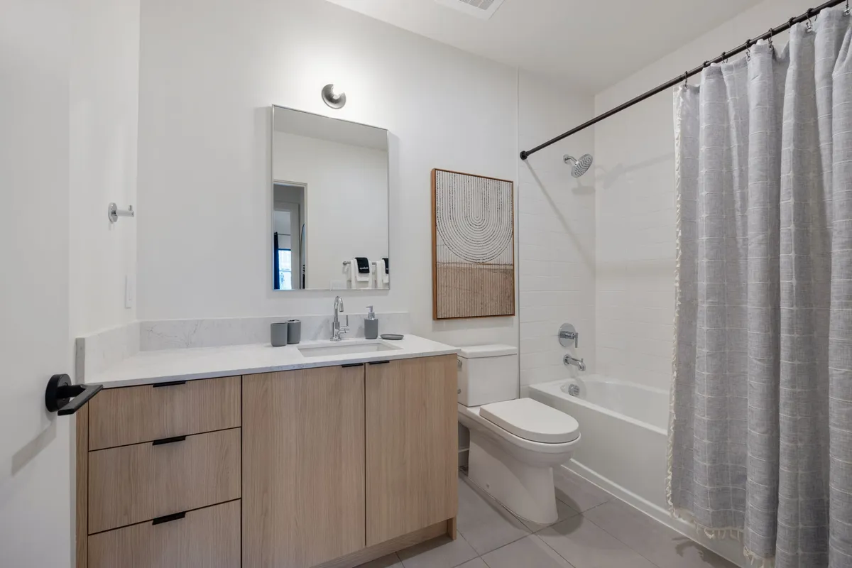 This bathroom features a vanity with a sink, a large mirror, and a bathtub, creating a serene and spa-like environment perfect for unwinding at the end of the day. The fixtures are modern and the space is bright, reflecting the dual focus on comfort and style.