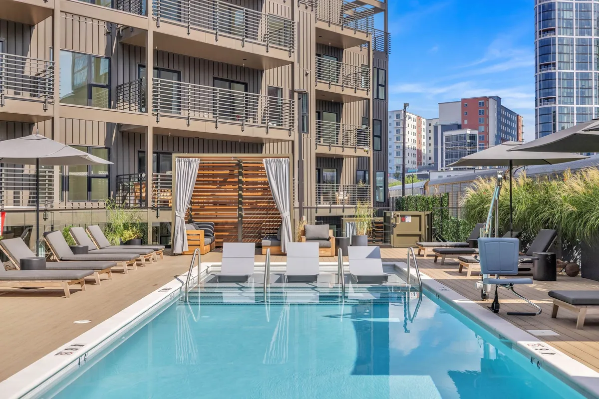 A sparkling swimming pool surrounded by lounge chairs and umbrellas, with the building facade visible in the background. The setup invites relaxation, socializing, and unwinding after a productive workday, reflecting a resort-style amenity.