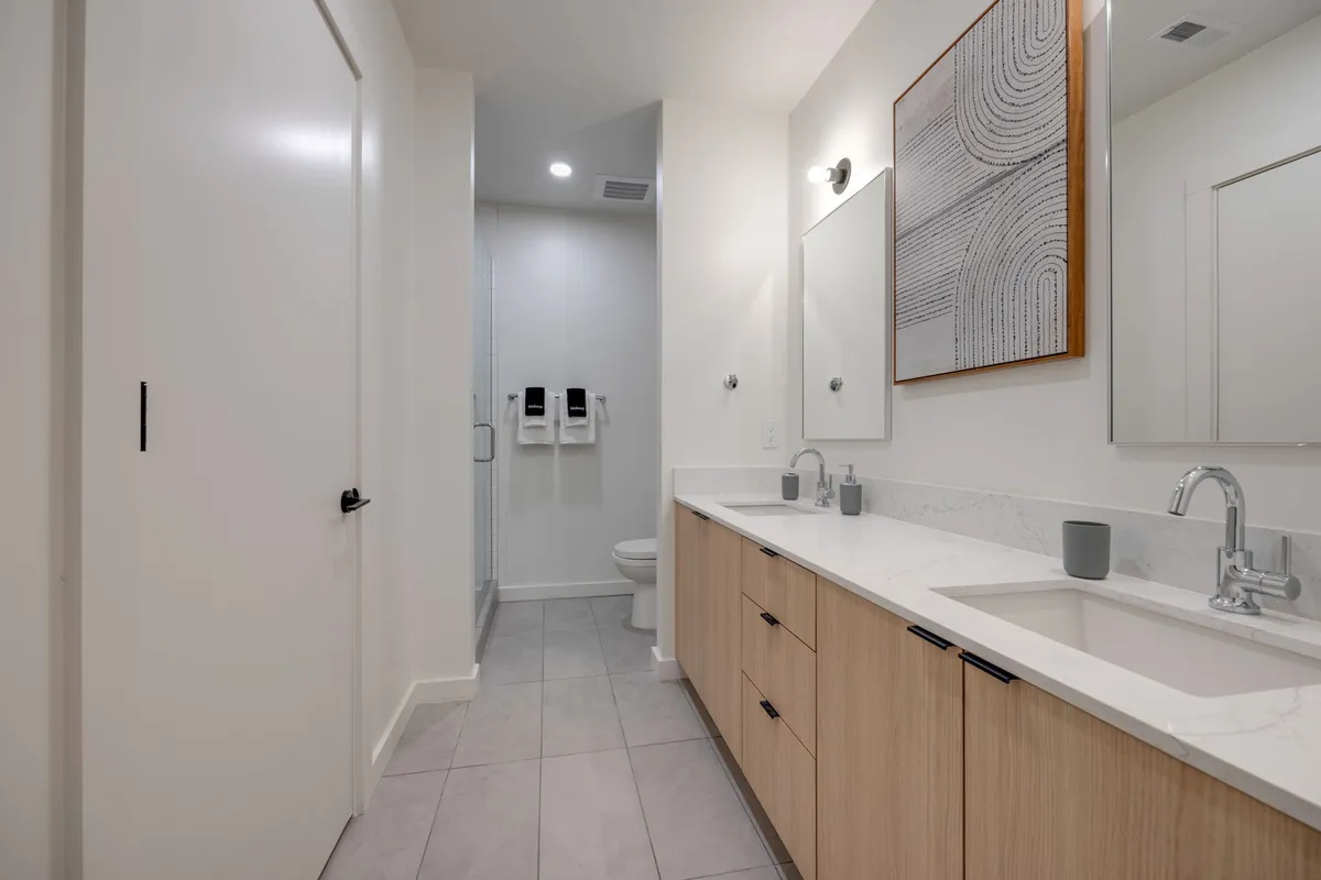 A sleek, modern double vanity bathroom with large mirrors and minimalist cabinetry. The space is bright, clean, and organized, exemplifying professional management and consistent hospitality standards. This setting is especially relevant for guests who value well-appointed bathrooms and daily comforts.