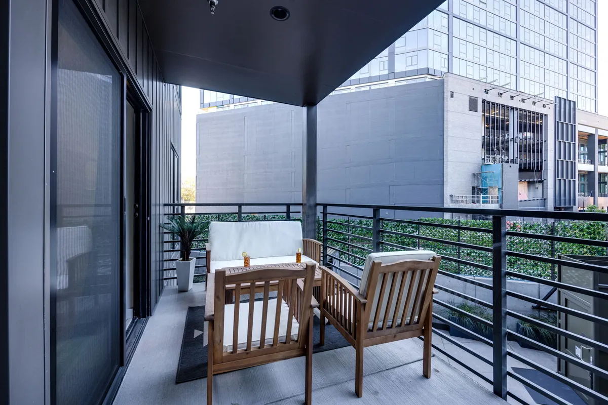 A tranquil balcony with a wooden furniture set, potted plants, and a city outlook, inviting guests to enjoy morning coffee or sunset cocktails while soaking up the urban energy.